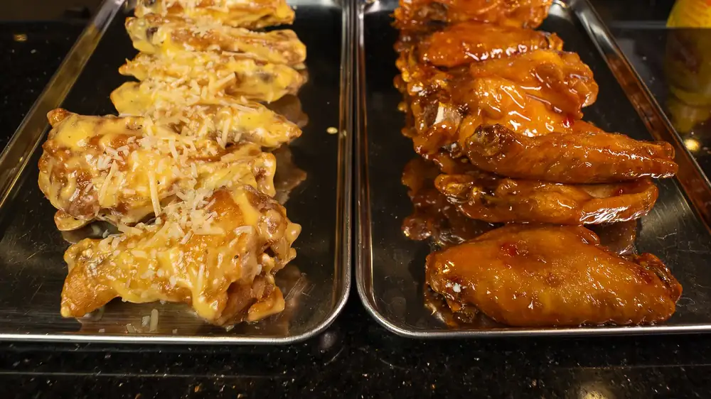 Two trays of house smoked wings, one tossed in garlic parmesan and one in a glossy orange sauce
