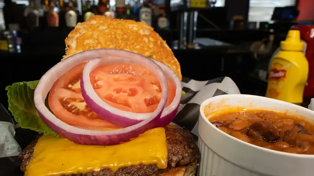 A cheeseburger with lettuce, tomato and red onion, with a cup of baked beans on the side, at 212
