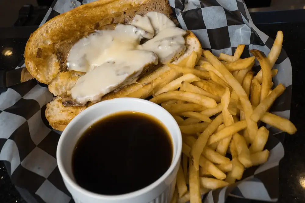 A brisket French dip with a cup of au jus and fries at 212