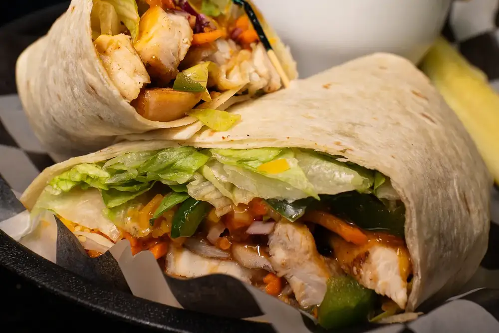 A chicken wrap cut in half with coleslaw and a dill pickle at 212