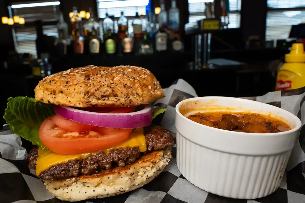 A cheeseburger with a cup of baked beans on checkered paper at 212
